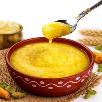 Yellow soup in a red bowl with a spoon, surrounded by turmeric roots and cardamom pods on a white background.